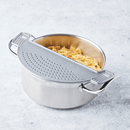 Stalen kookpot met pasta en afgietdeksel dat de pot half bedekt op grijs keukenblad 