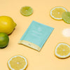 Groen zakje Brauzz afwasmiddel op gele tafel met citroenen en limoenen