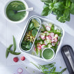 Lunchbox met oosterse salade met noedels en radijs met groen sausje op een witte tafel