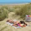 Opblaasbaar katoenen kussen multicolour op multicolour strandlaken met vrouw erop met de duinen op de achtergrond 