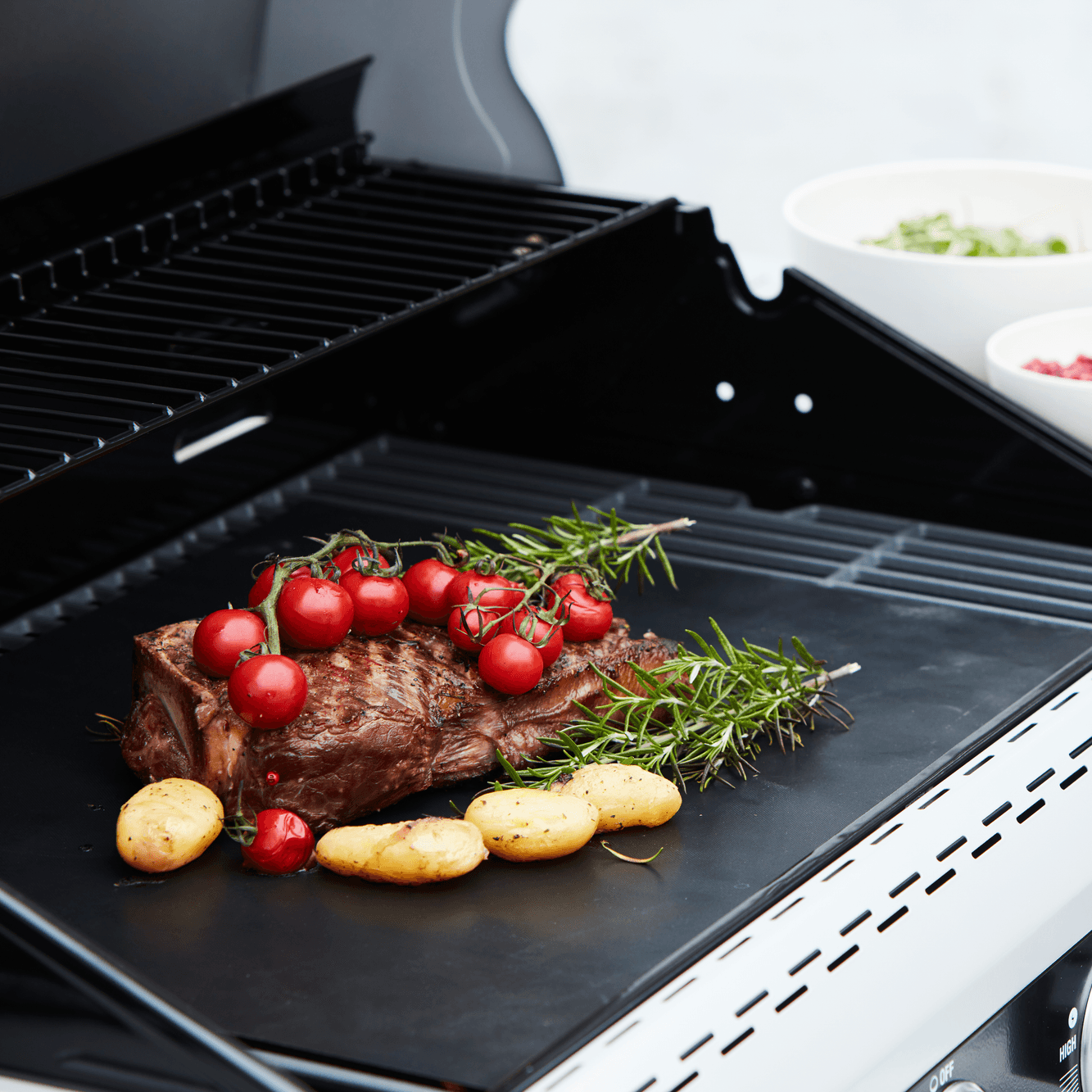 Zwarte grillmat op de BBQ met aardappelen vlees met rozemarijn en trostomaatjes