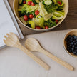 Houten saladebestek op een tafel met beige tafellaken en een kom met salade