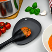 Zwarte afleglepel met lepel naast bord met paprika soep